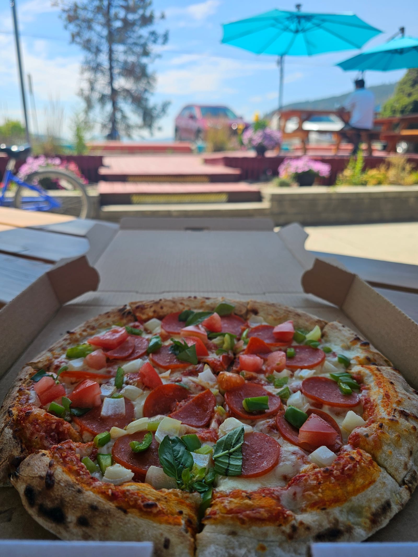 A fresh thin-crust pepperoni pizza in the box at Lu Lou's, with the lakeside patio umbrellas behind it