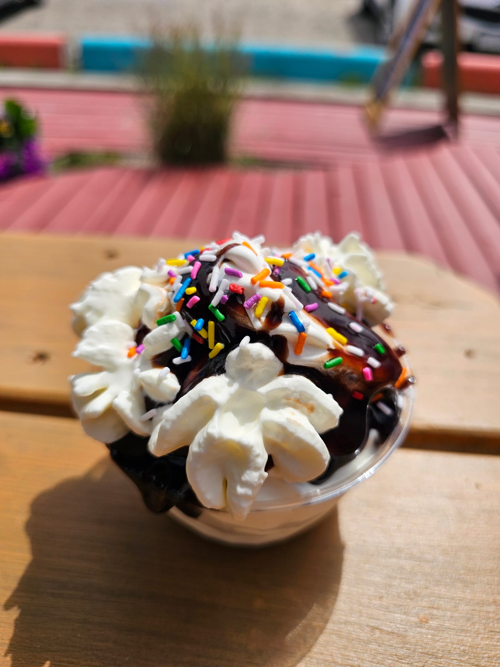 A chocolate sundae in a takeaway cup, soft-serve, whipped cream, chocolate sauce, rainbow sprinkles