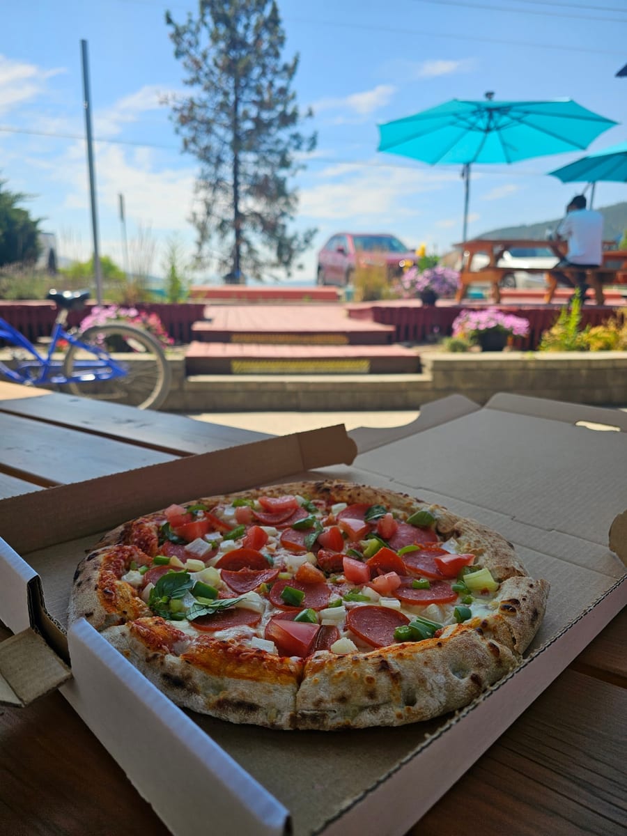 Thin-crust pepperoni pizza in the box on a lakeside picnic table