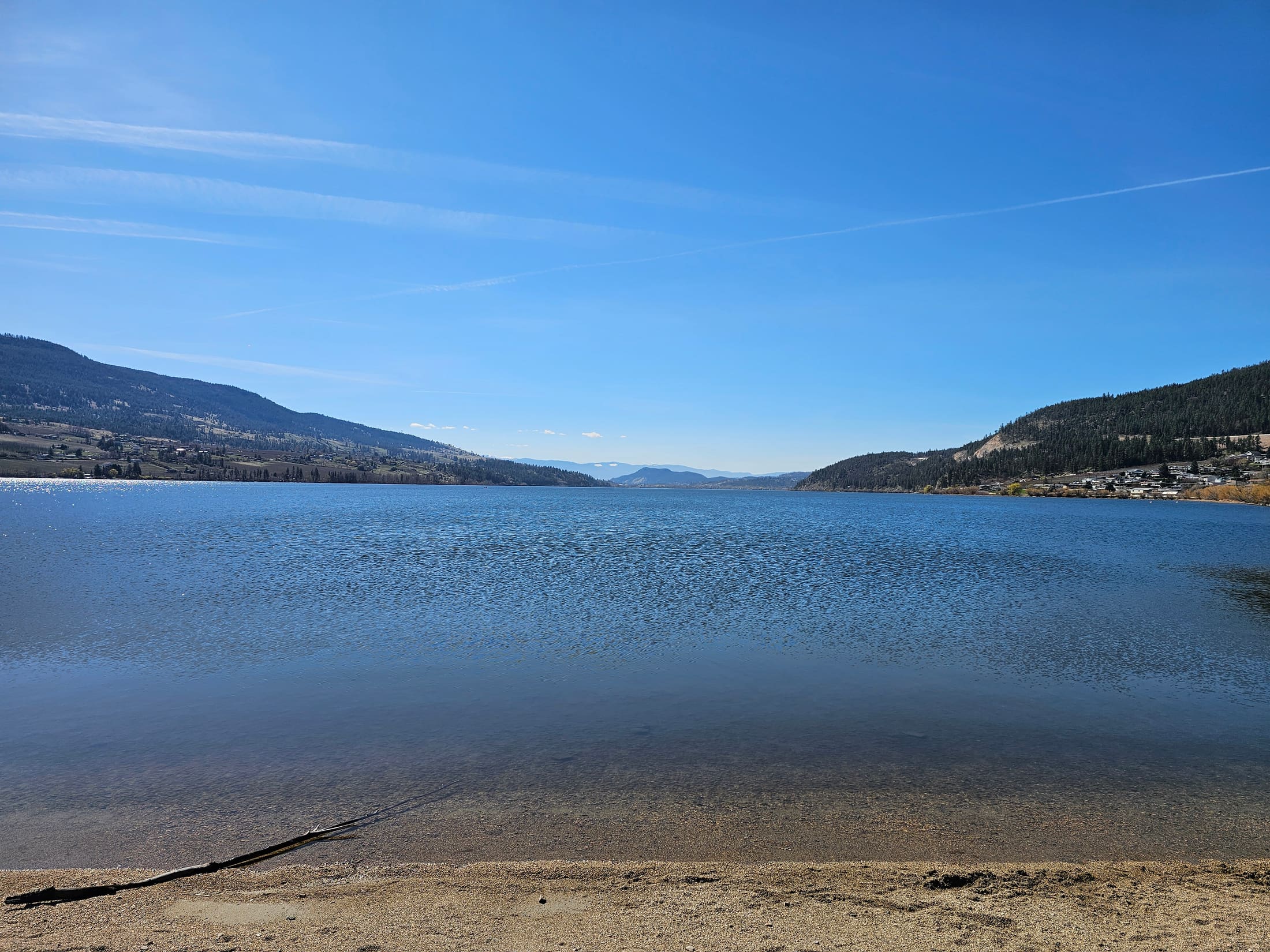 Calm water on Wood Lake in Oyama, BC, mountains reflected on a clear day, a few steps from Lu Lou's Lakeside Grill